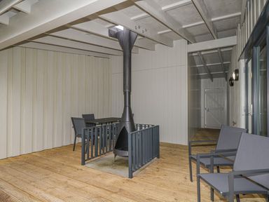 A covered outdoor patio with wooden flooring metal chairs a table and a central fireplace at Red Deer Lodge in Feshiebridge near Aviemore