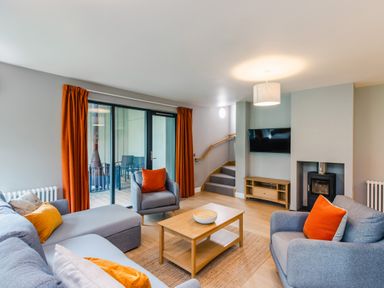 A living room with gray sofas orange cushions a wooden coffee table a wall-mounted TV and sliding glass doors at Red Deer Lodge in Feshiebridge near Aviemore