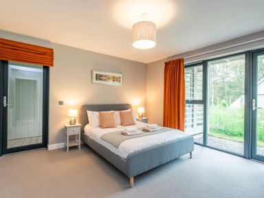 A bedroom with a double bed bedside tables lamps and large windows with orange curtains at Red Deer Lodge in Feshiebridge near Aviemore