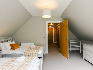 A bedroom with two single beds a door leading to a hallway and a dresser at Red Deer Lodge in Feshiebridge near Aviemore