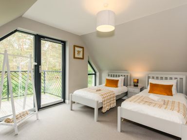 A bedroom with two single beds with orange pillows near a balcony door and a white clothes rack at Red Deer Lodge in Feshiebridge near Aviemore