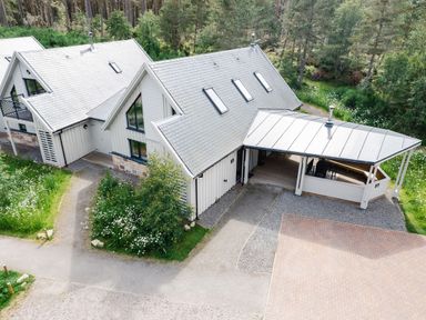A pair of white houses with pitched roofs surrounded by trees and greenery at Red Deer Lodge in Feshiebridge near Aviemore