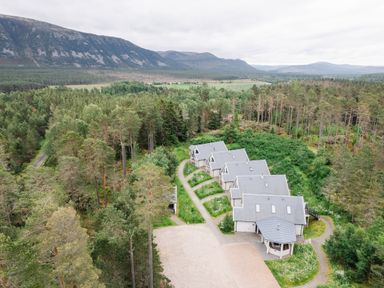 A row of houses surrounded by trees and mountains at Red Deer Lodge in Feshiebridge near Aviemore