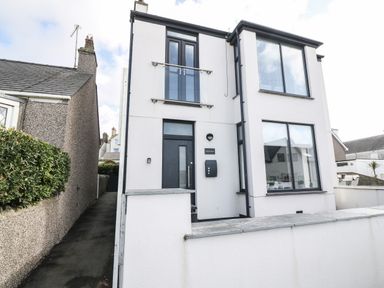 A modern two-story house with white walls large windows and black door at Arlanfor in Rhosneigr