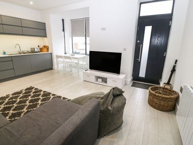 An open plan living space with a kitchen area dining table television sofa and black front door at Arlanfor in Rhosneigr
