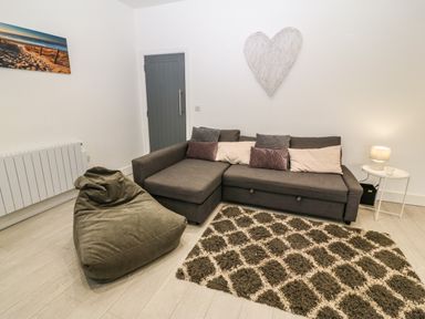 A living room with a gray sofa and pillows a bean bag chair a patterned rug a side table with a lamp and a wall decoration in the shape of a heart at Arlanfor in Rhosneigr
