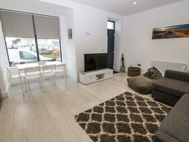 A living room with a sofa bean bag rug television and dining table with chairs at Arlanfor in Rhosneigr