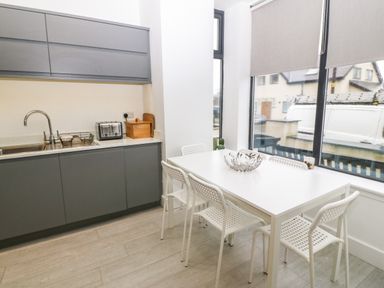 A kitchen with gray cabinets a white dining table with white chairs and large windows at Arlanfor in Rhosneigr