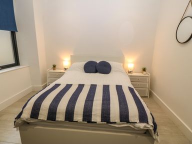A bedroom with a bed with striped blanket and round pillows two bedside tables with lamps and plants at Arlanfor in Rhosneigr