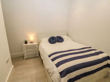 A bedroom with a bed covered with white and blue striped blanket two round blue pillows and a bedside table with a lamp and a small plant at Arlanfor in Rhosneigr