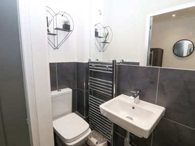A bathroom with a toilet a white sink a chrome towel radiator and a heart-shaped wall shelf at Arlanfor in Rhosneigr