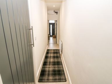 A narrow hallway with a plaid carpet runner and a grey door at Arlanfor in Rhosneigr