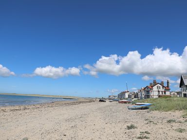 A sandy beach with boats on the shore and houses along the edge under a blue sky with clouds at Arlanfor in Rhosneigr
