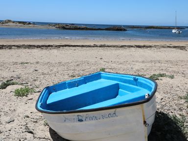 A small boat on a sandy beach with rocks and ocean in the background at Arlanfor in Rhosneigr