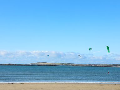 A beach with kitesurfers on the water and hills in the background at Arlanfor in Rhosneigr