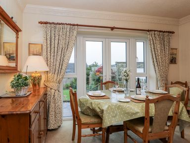 A dining room with set table by glass doors and wooden furniture at Sanderling in Scalby