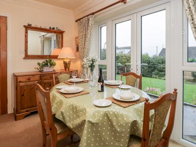 A dining room with a table set for four near glass doors overlooking a garden at Sanderling in Scalby