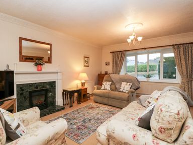 A living room with floral sofas a fireplace a lamp a rug and a large window at Sanderling in Scalby