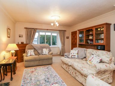 A living room with two sofas a wooden cabinet a table lamp and patterned curtains at Sanderling Scalby