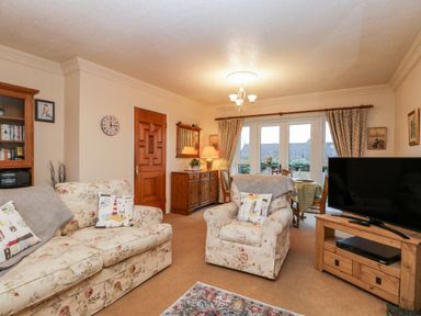 A living room with floral sofas a wooden cabinet and a television at Sanderling in Scalby