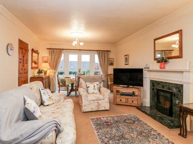 A living room with floral sofas a television on a wooden stand and a fireplace at Sanderling in Scalby