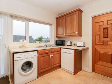 A kitchen with wooden cabinets a washing machine dishwasher microwave kettle toaster and a wooden door at Sanderling in Scalby