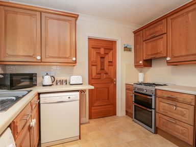 A kitchen with wooden cabinets a dishwasher a microwave a kettle a toaster a stove and a wooden door at Sanderling in Scalby