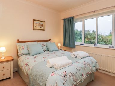 A bedroom with a floral bedspread and pillows bedside tables with lamps and a window with blue curtains at Sanderling in Scalby