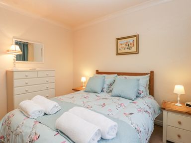 A bedroom with a double bed with floral bedding and rolled towels on it with bedside tables and lamps at Sanderling in Scalby