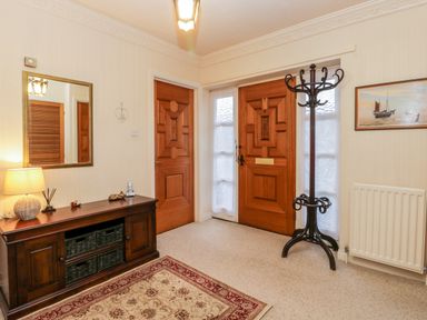 An entryway with wooden front and interior doors a wooden cabinet with a lamp and mirror a coat rack and a rug at Sanderling in Scalby