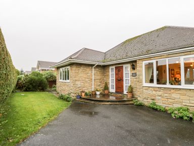 A stone house with a wooden front door potted plants a driveway and a grass lawn at Sanderling in Scalby