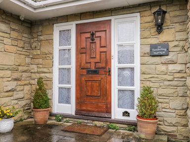 A wooden front door with decorative glass panels on a stone wall with potted plants outside at Sanderling in Scalby
