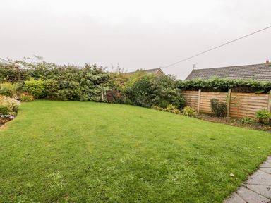 A backyard with green grass and shrubs along a wooden fence at Sanderling in Scalby