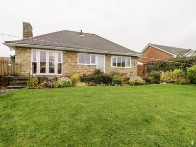 A garden with green grass and plants in front of a stone house with windows and a door at Sanderling Scalby