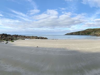 A sandy beach with rocky outcrops and calm sea under a partly cloudy sky at Cwch Gwenyn in Llanfachraeth