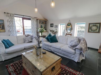 A living room with two white sofas and a wooden coffee table with a bottle in a bucket and glasses at Cwch Gwenyn in Llanfachraeth