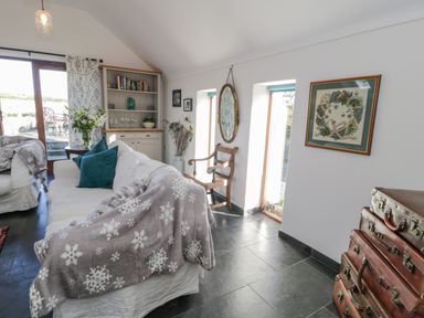 A living room with white sofas blue pillows bookshelf and stacked suitcases at Cwch Gwenyn in Llanfachraeth