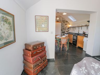 A kitchen and dining area with stacked vintage suitcases and framed pictures on white walls at Cwch Gwenyn in Llanfachraeth