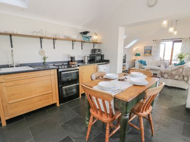 A kitchen with a wooden dining table set for four and a living area with sofas and a coffee table at Cwch Gwenyn in Llanfachraeth