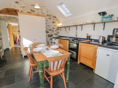 A kitchen with wooden cabinets a dining table with four chairs and stone walls at Cwch Gwenyn in Llanfachraeth