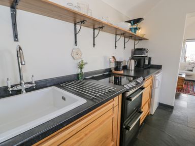 A kitchen with a sink stove oven microwave and wooden cabinets at Cwch Gwenyn in Llanfachraeth