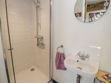 A bathroom with a glass shower enclosure a white sink a round mirror and a purple towel at Cwch Gwenyn in Llanfachraeth