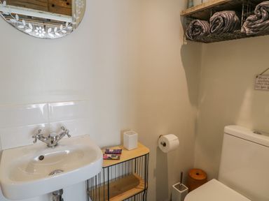 A bathroom with a sink and faucet a small shelf with items rolled towels on a hanging basket and a toilet with a toilet paper holder at Cwch Gwenyn in Llanfachraeth
