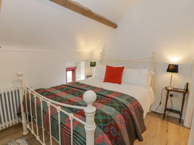A bedroom with a white metal bed a colorful blanket orange pillow two bedside lamps and wooden flooring at Cwch Gwenyn in Llanfachraeth