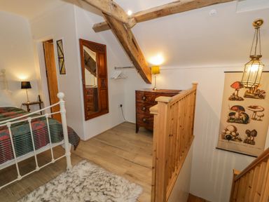 A bedroom with a bed a wooden chest of drawers a wall mirror and a hanging light at Cwch Gwenyn in Llanfachraeth