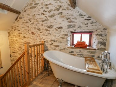 A bathroom with a freestanding bathtub near a stone wall and a window with folded towels on the sill at Cwch Gwenyn in Llanfachraeth