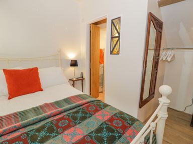 A bedroom with a bed a side table a lamp a wall mirror and hangers at Cwch Gwenyn in Llanfachraeth