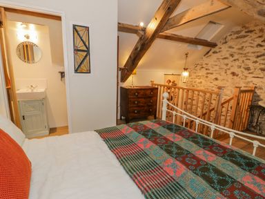 A bedroom with a bed blanket a wooden dresser exposed beams and stone wall at Cwch Gwenyn in Llanfachraeth