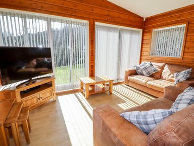 A living room with two brown sofas a wooden coffee table a flat screen tv and large windows with vertical blinds at Watersview Lodge Rudyard near Leek