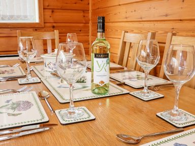A dining table set with wine glasses plates utensils and a bottle of white wine at Watersview Lodge in Rudyard near Leek